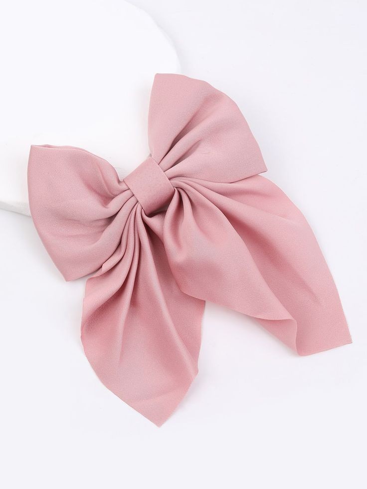 Large pink fabric bow with a simple knot in the center, placed on a white surface.