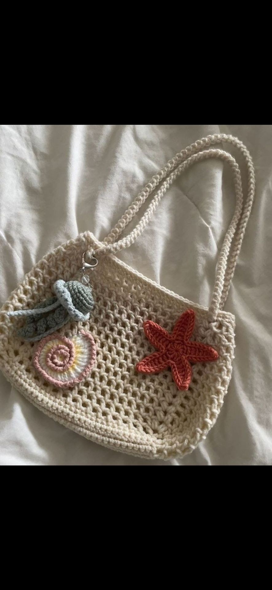 Handmade crochet bag with starfish and spiral shell designs on a white fabric background.