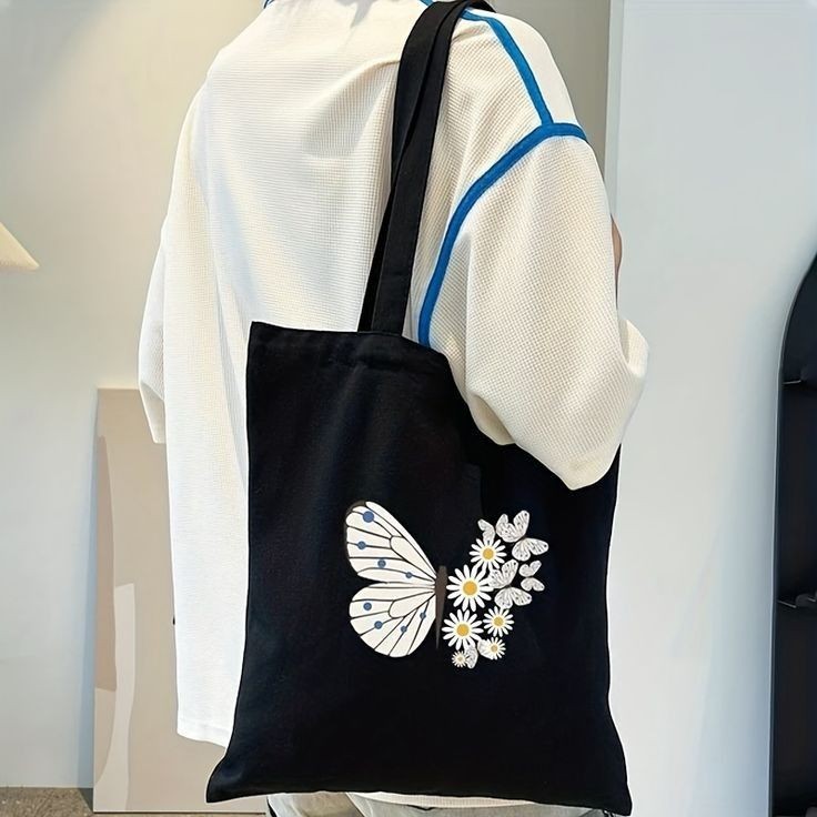 Person wearing a black tote bag with butterfly and floral design.